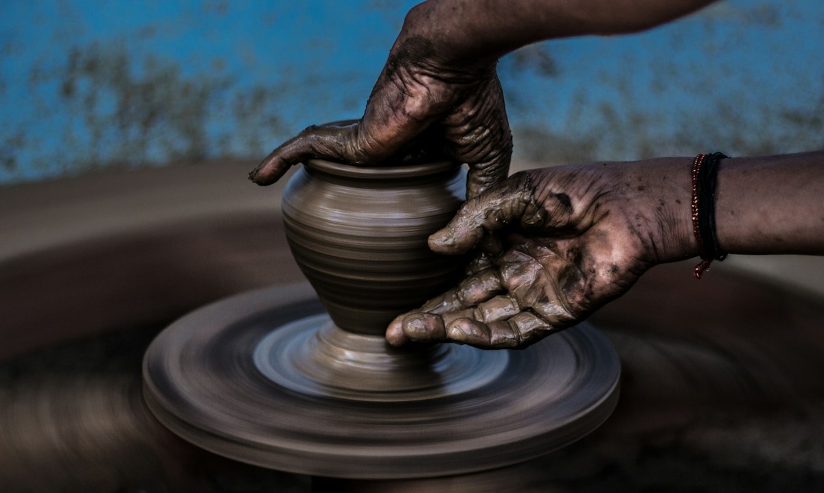 Hands shaping a clay vessel on a pottery wheel.
